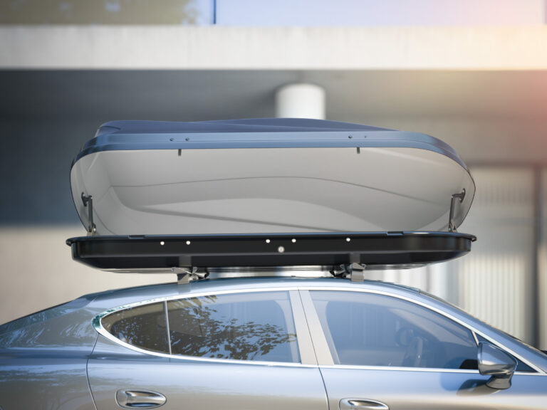 Auto so strešným boxom tesne pred vjazdom do nízkej garáže, ilustrujúce riziko nárazu.